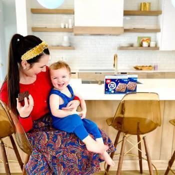 A woman smiling at the child in her lap, while holding a Fiber One brownie in her free hand. - Link to social post