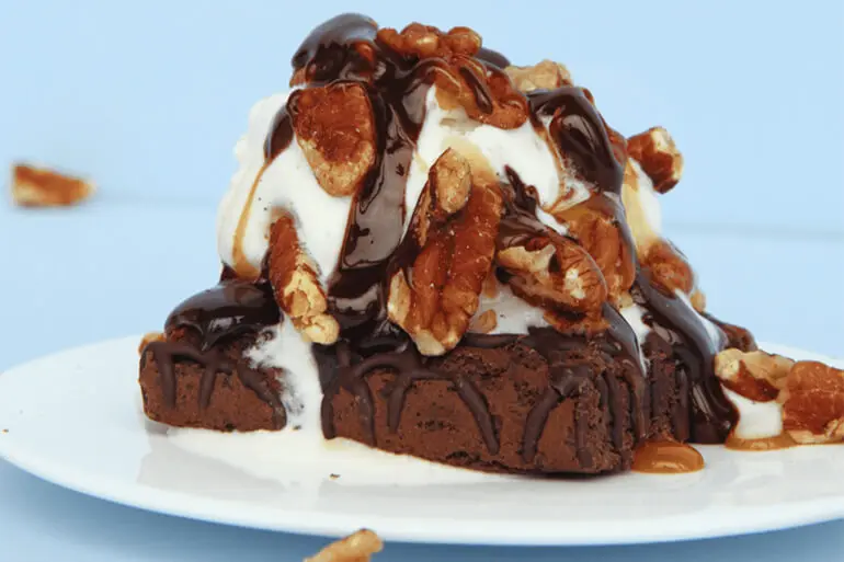 Fiber One Turtle Brownie Onedae Recipe topped with ice cream, caramel, chocolate sauce and nuts on a white plate with a blue background